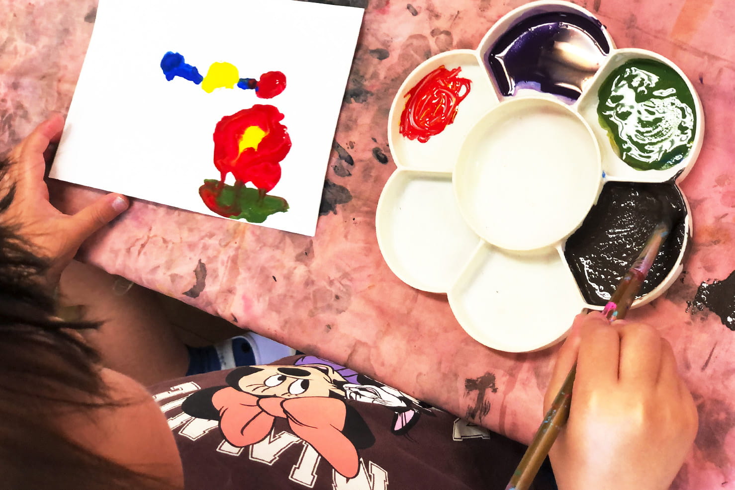 絵の具パレットを使いながら、子どもが白い紙にカラフルな絵を描いている場面