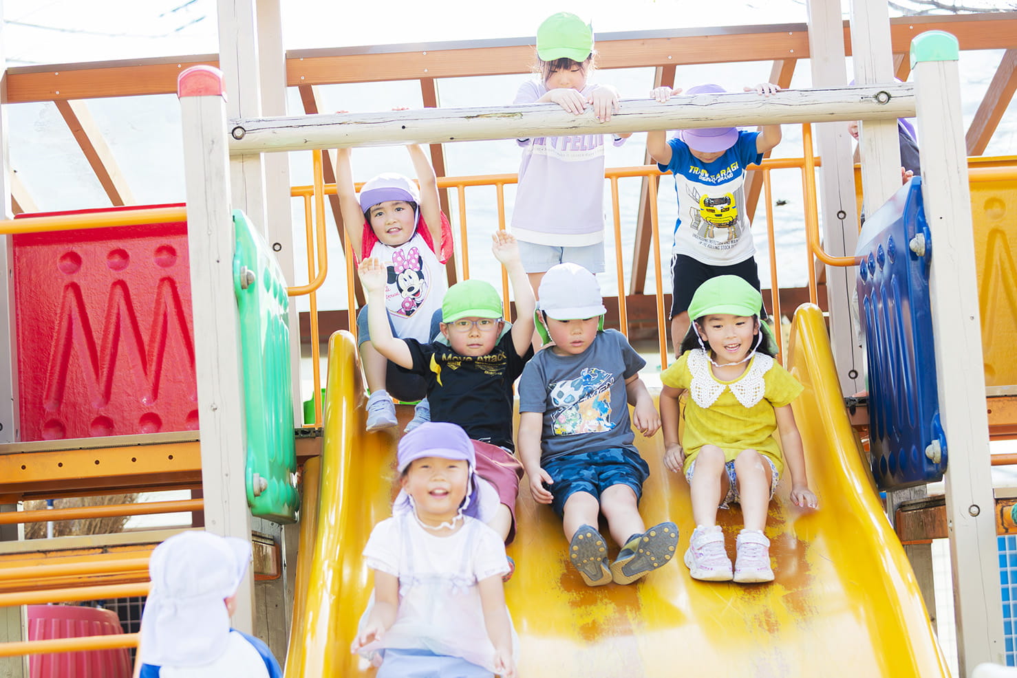 遊具のすべり台の上で、子どもたちが順番に滑りながら楽しんでいる様子