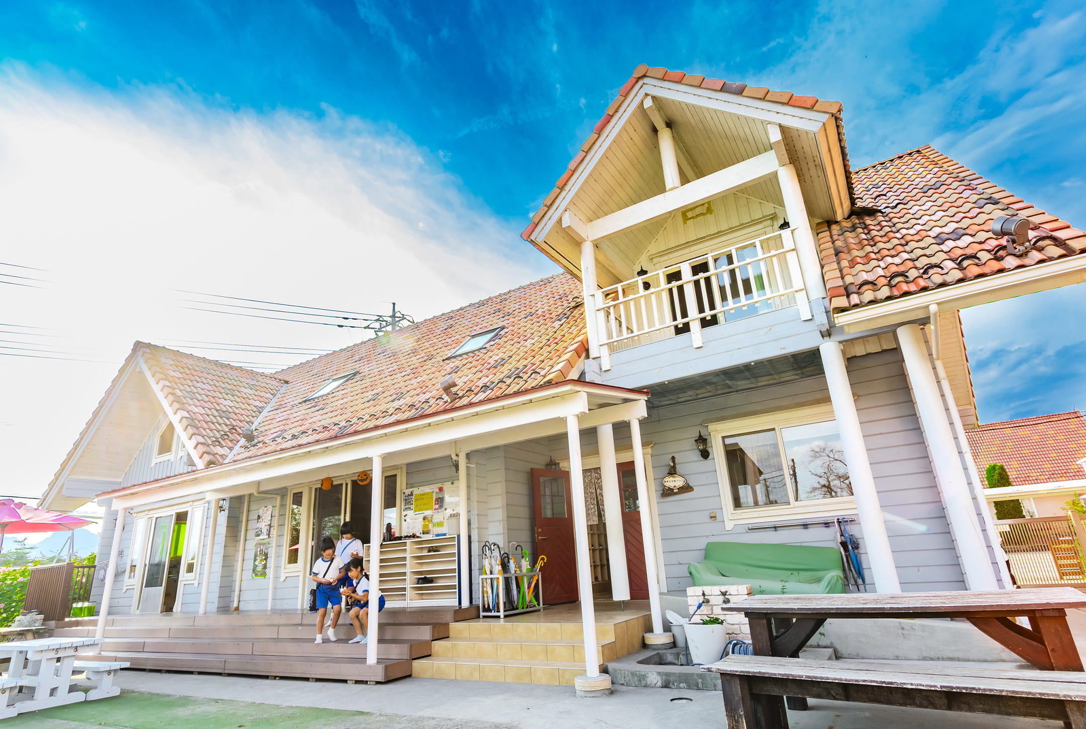 赤い屋根が印象的な園舎とウッドデッキ。子どもたちが楽しそうに過ごす、温かみのあるあさひ学童クラブ外観。