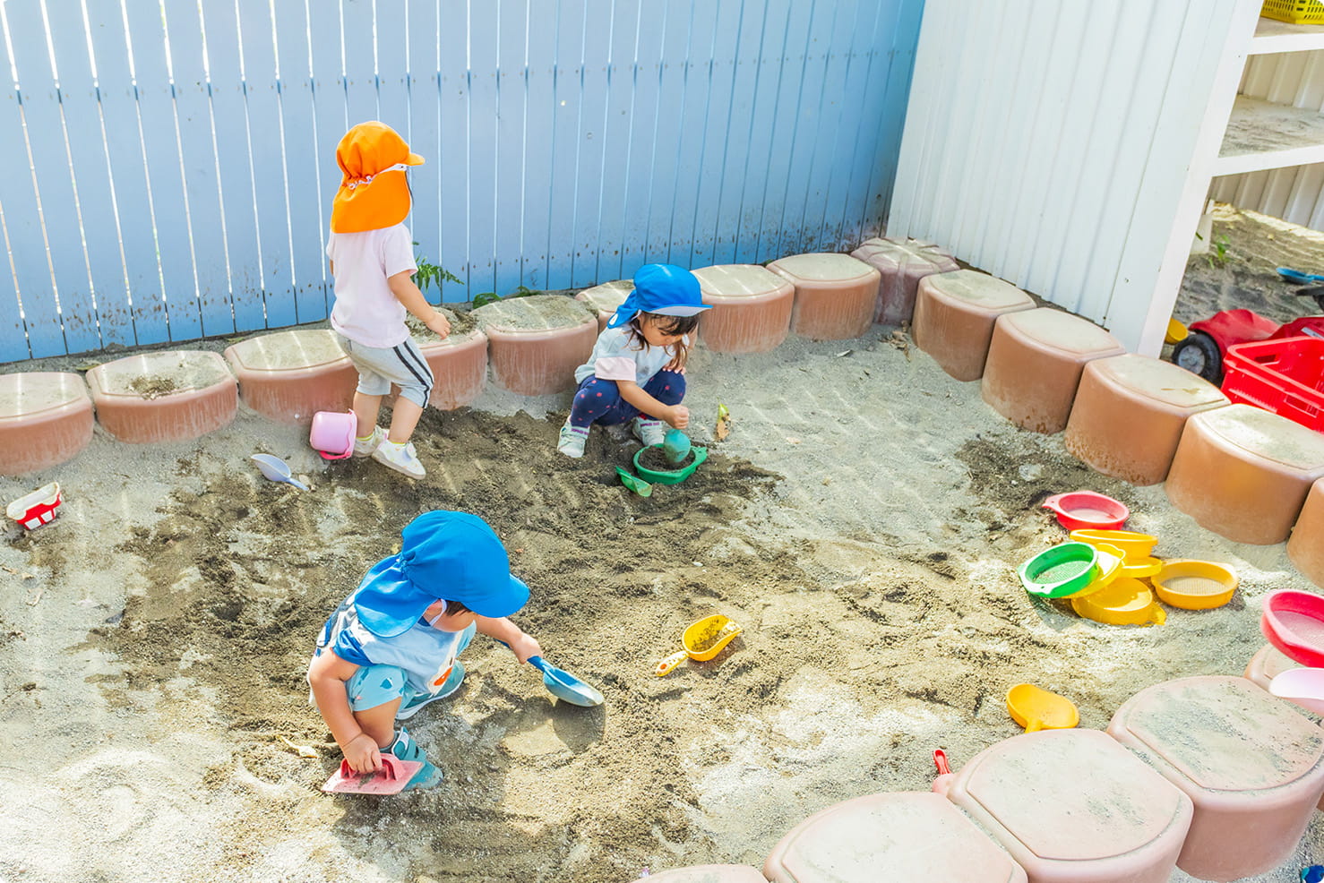 子どもたちが砂場でスコップやバケツを使って砂遊びをしている様子