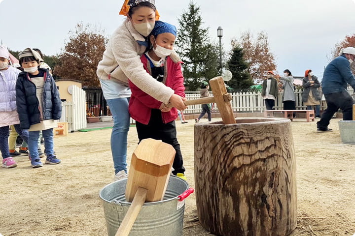 餅つきを体験する園児と保護者
