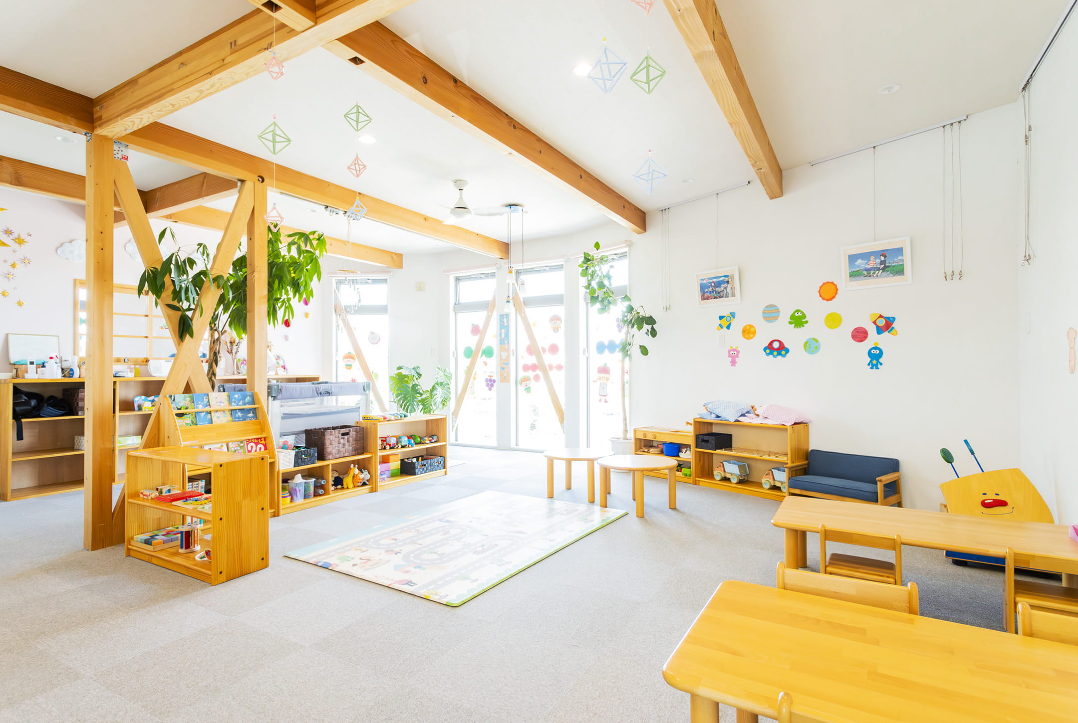 木の温もりを感じる広々とした室内に、机や棚、おもちゃが揃った保育室の風景
