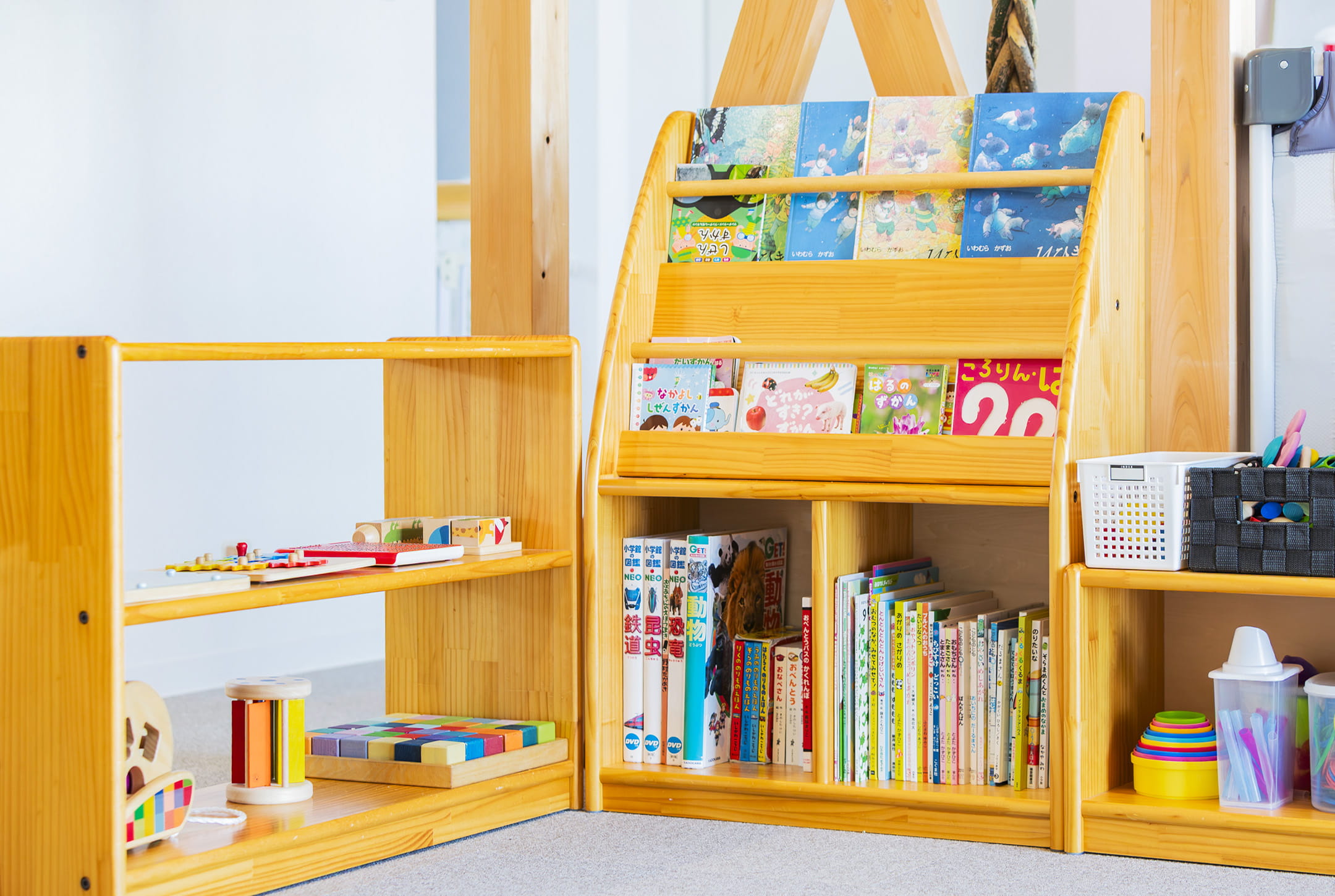 木製の棚に絵本やおもちゃが整然と並ぶ、子ども向けの遊びと読み聞かせのコーナー