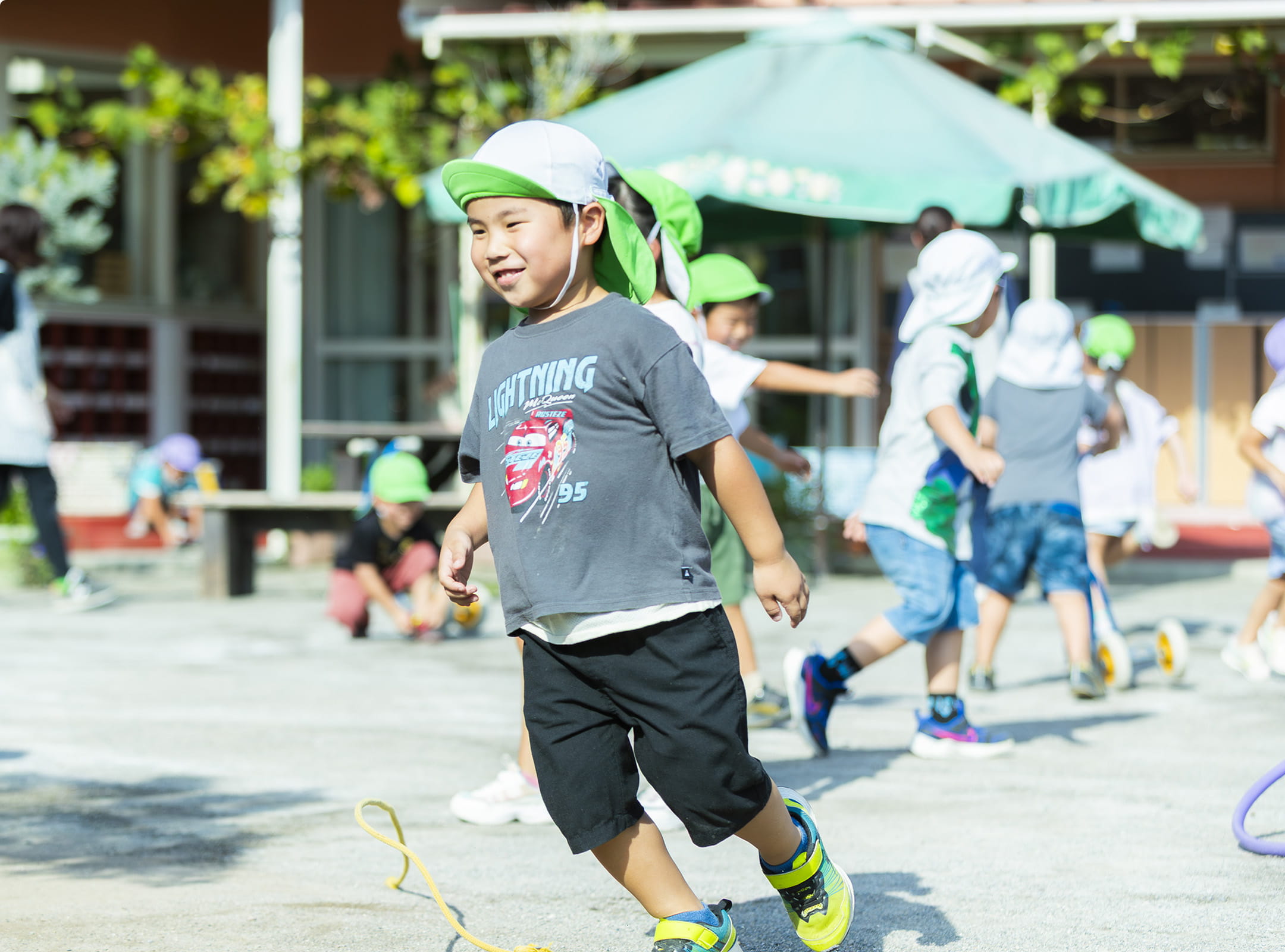 緑の帽子をかぶった子どもたちが園庭で元気に遊んでいる様子